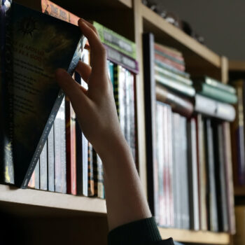 Hand reaching to take a book off a shelf of books