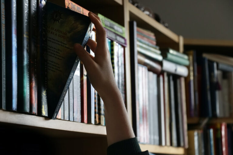 Hand reaching to take a book off a shelf of books