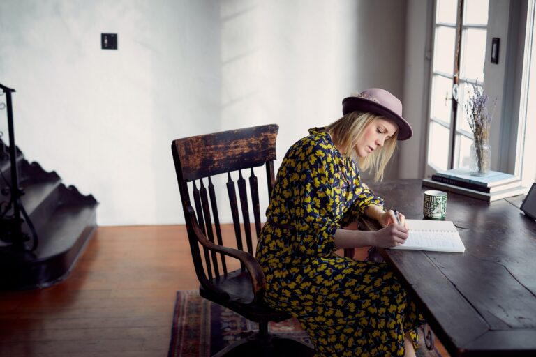 artist writing copy woman wearing a hat sitting at a desk writing