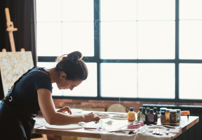 woman leaning over desk making art