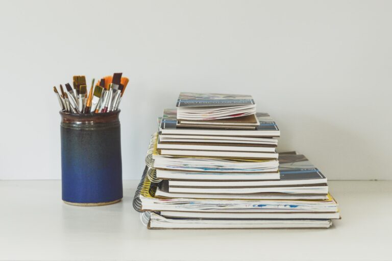 Marketing Image of a pile of art books next to a tin of brushes